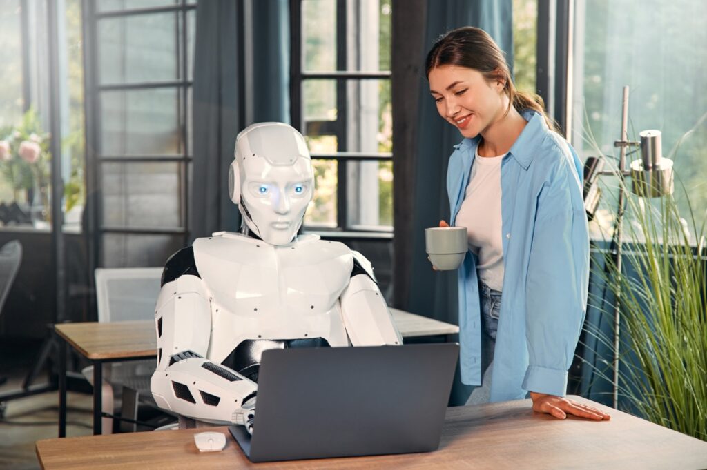 A photo of a robot and a woman in front of a computer.