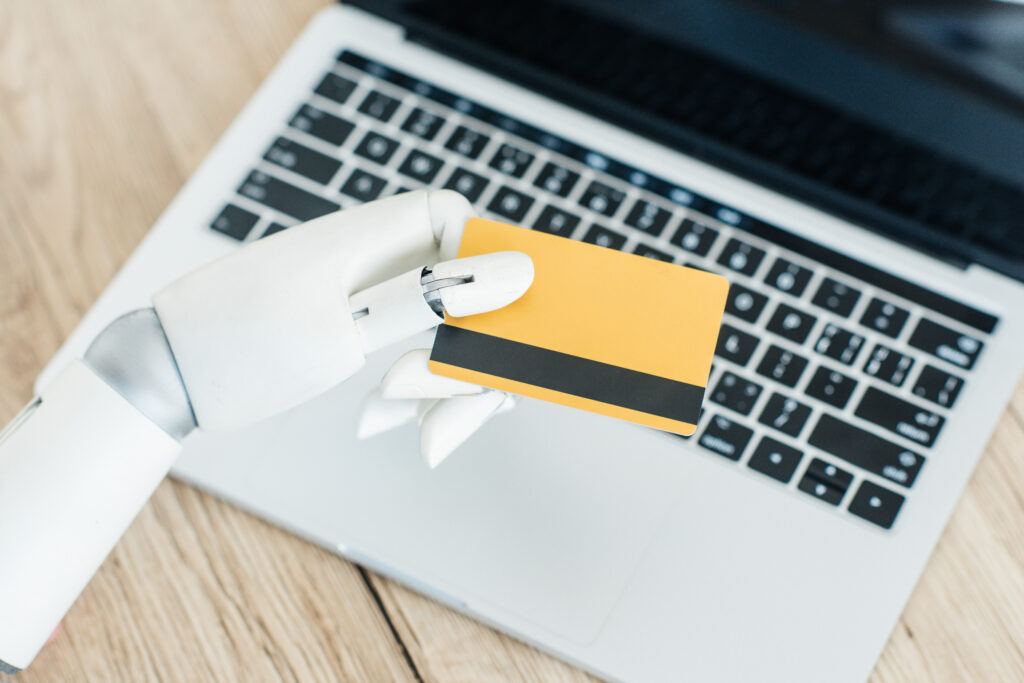 close-up view of robot holding credit card above laptop on wooden table
