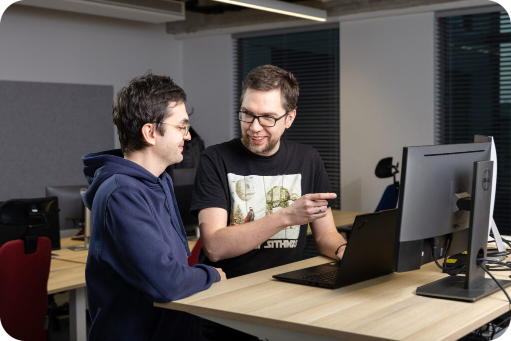 A photo of 2 Spyrosoft AdTech employees talking in front of a computer screen.